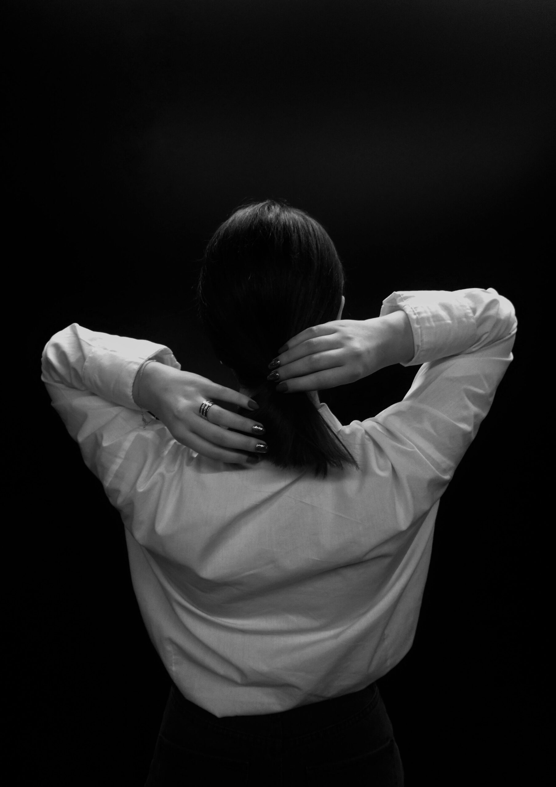 A stylish black and white portrait of a person adjusting their hair from behind.