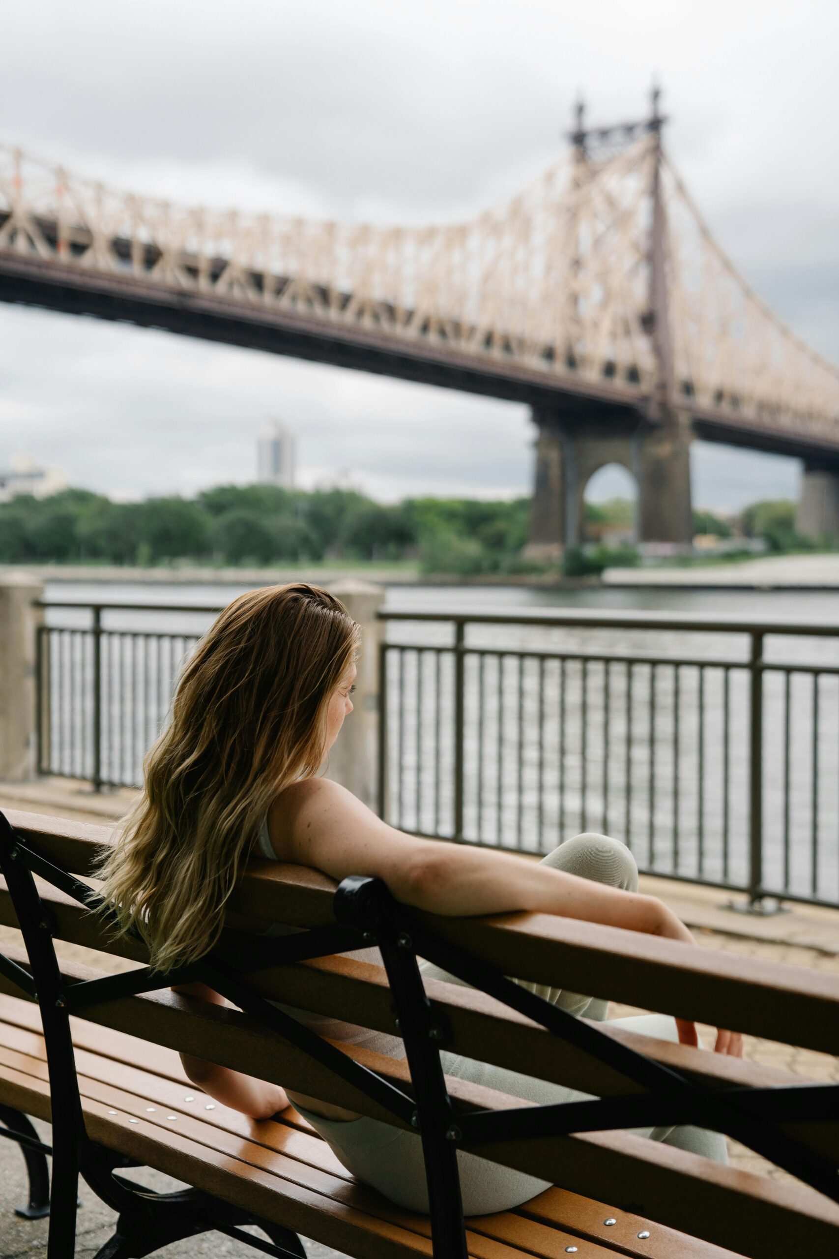 Woman sitting on a bench enjoying the view of a famous bridge over a river.
